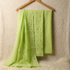 Green applique fabric set with intricate patterns draped over a wooden hanger against a textured beige background.