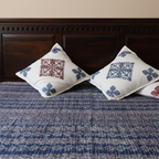 Two embroidered pillows on a blue patterned applique bedspread with a wooden headboard.