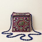 Decorative small ethnic sling bag with elephant design and blue pom-pom strap on a white background